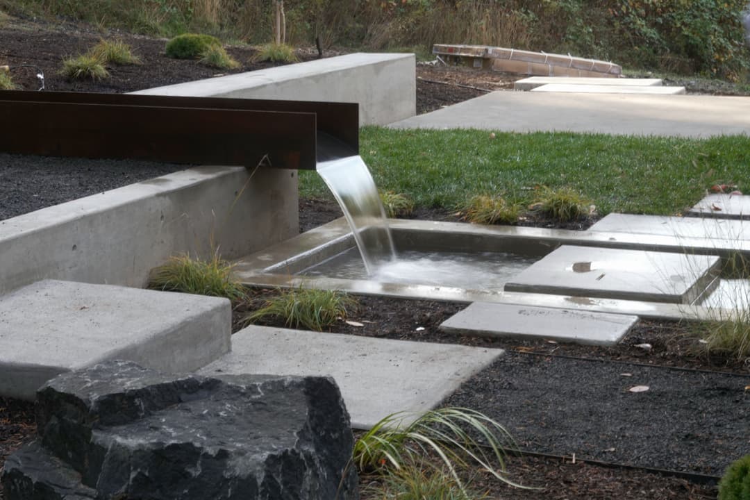 Water feature with modern stone pathway and grass in a landscaped garden setting.