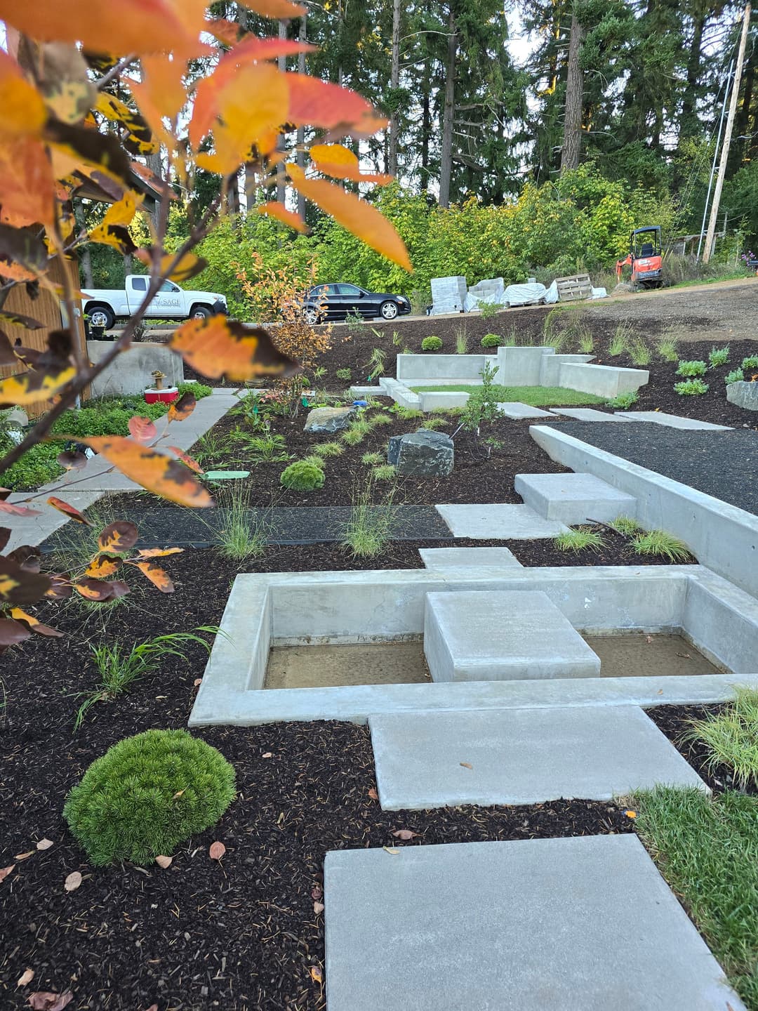 Modern garden landscape with concrete pathways, stone features, and colorful autumn foliage.