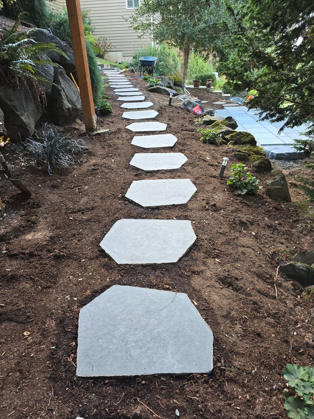 Stone pathway leading through a landscaped garden with rocks and plants on either side.