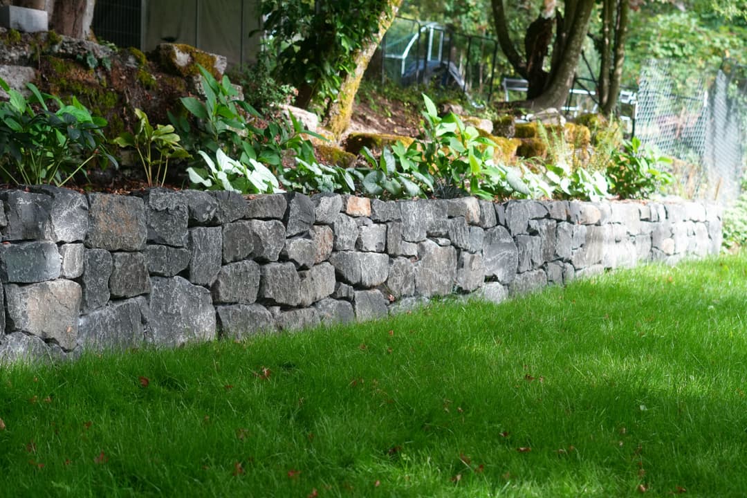 Stone retaining wall with lush greenery and grass in a landscaped garden setting.