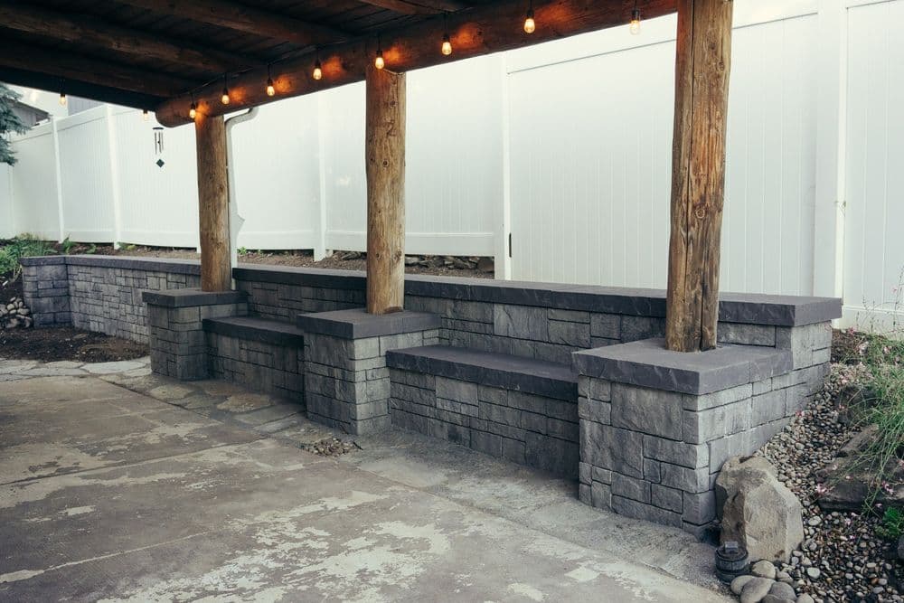 Outdoor stone seating area with grey block walls and wooden posts, under decorative string lights.