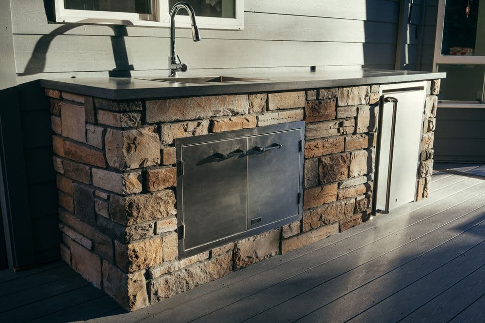 Outdoor kitchen with stone counter, stainless steel sink, and built-in storage. Perfect for entertaining.