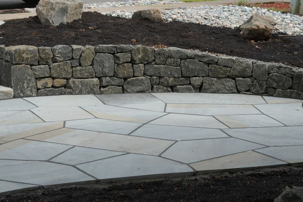 Beautifully designed stone patio with a well-structured rock wall and surrounding gravel.