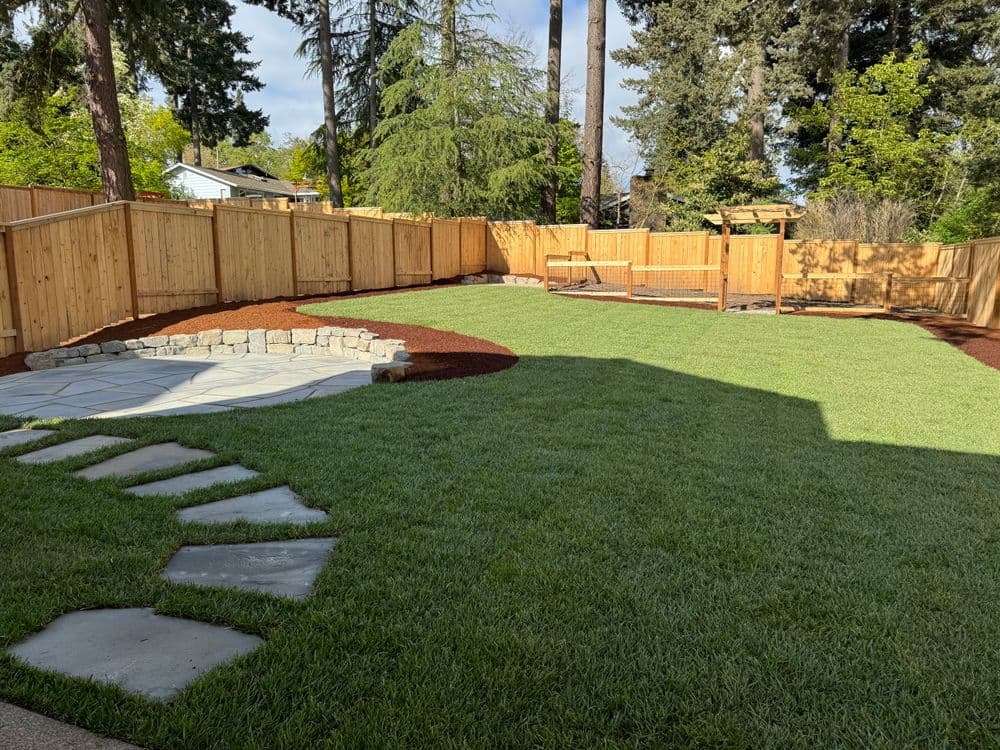 Lush green backyard with stone pathways, wooden fence, and shaded play area.