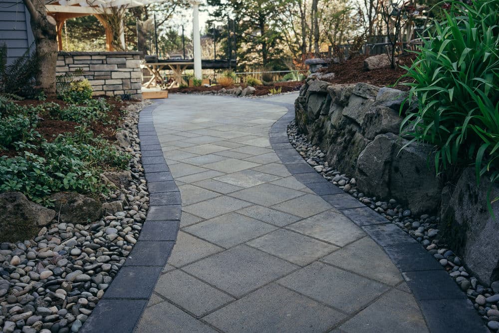 Winding stone pathway bordered by greenery and rocks in a landscaped garden setting.