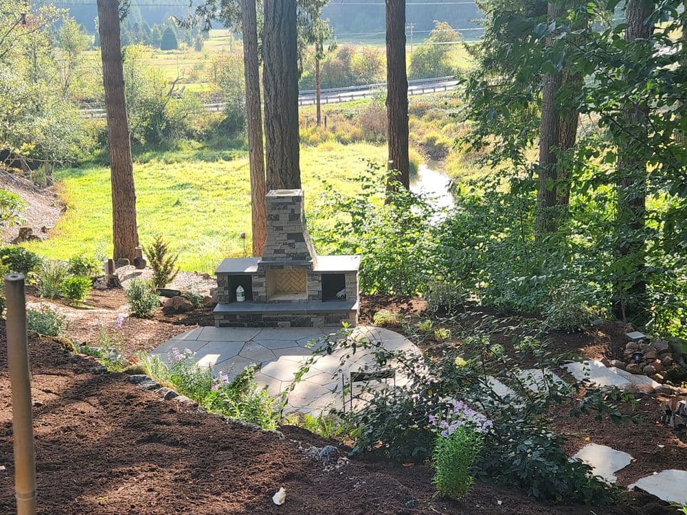 Scenic outdoor landscape with a stone fireplace, lush greenery, and a winding path.
