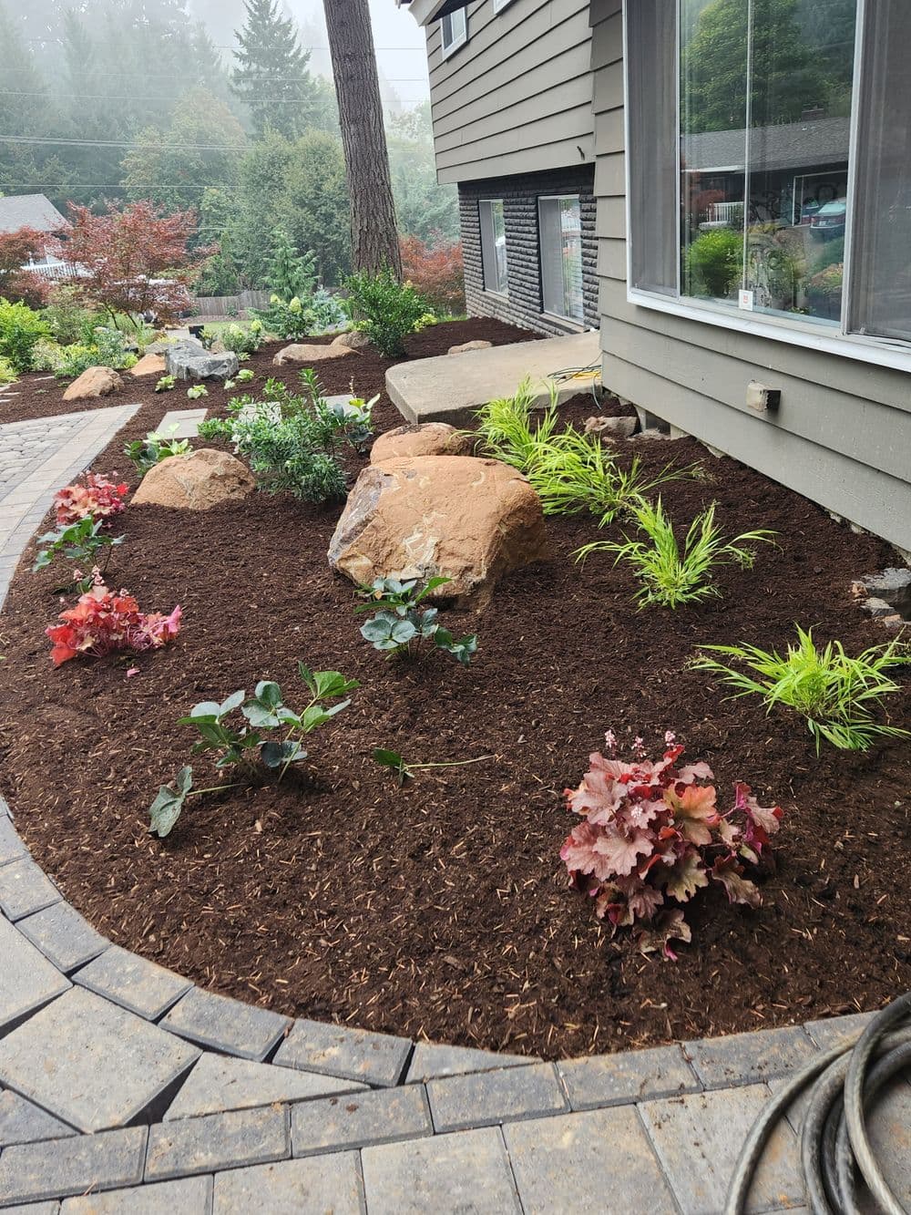 Lush garden landscape featuring rocks, mulch, and colorful plants near a home.