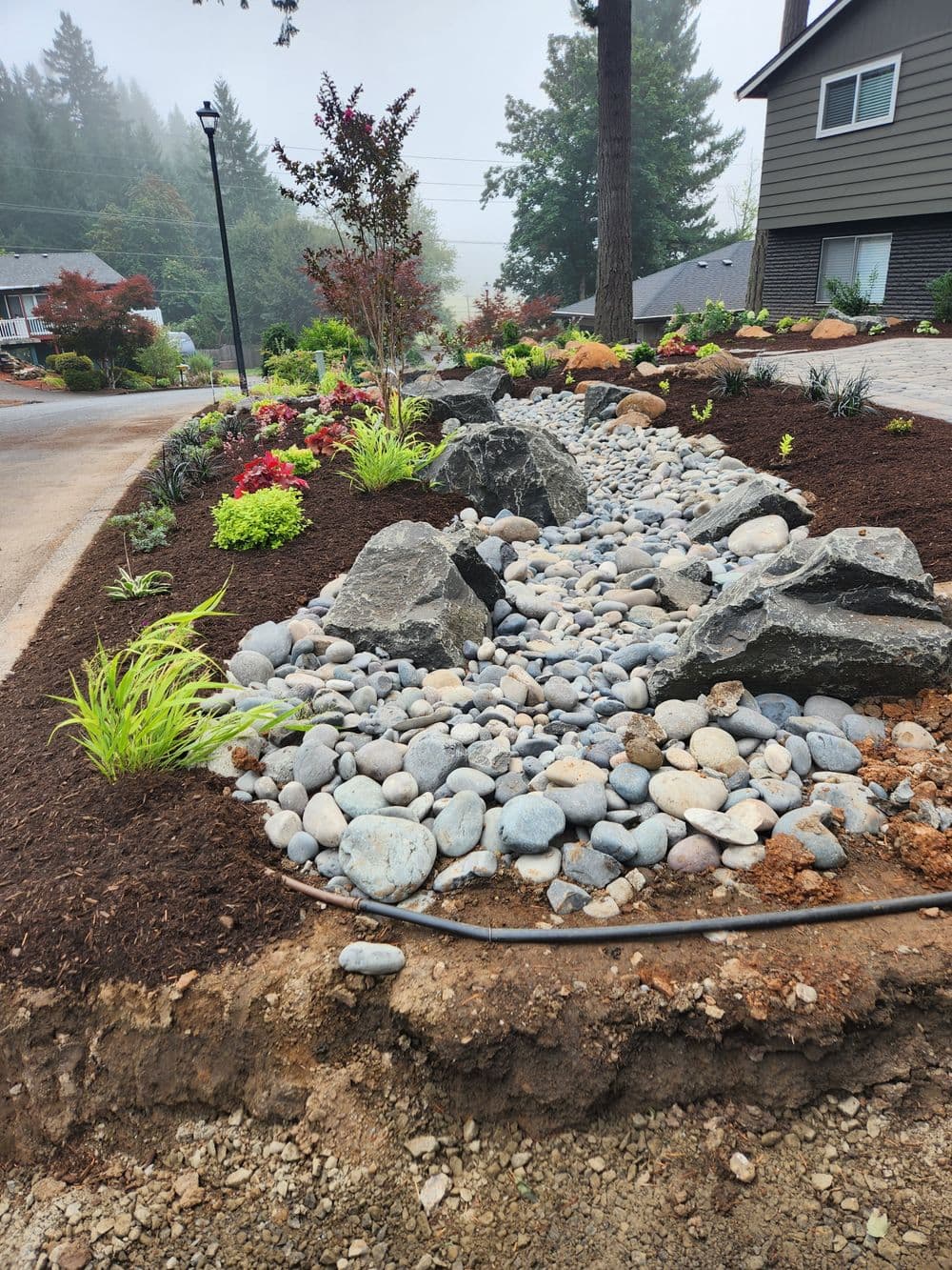 Landscape design featuring river rocks, shrubs, and plants in a residential front yard.