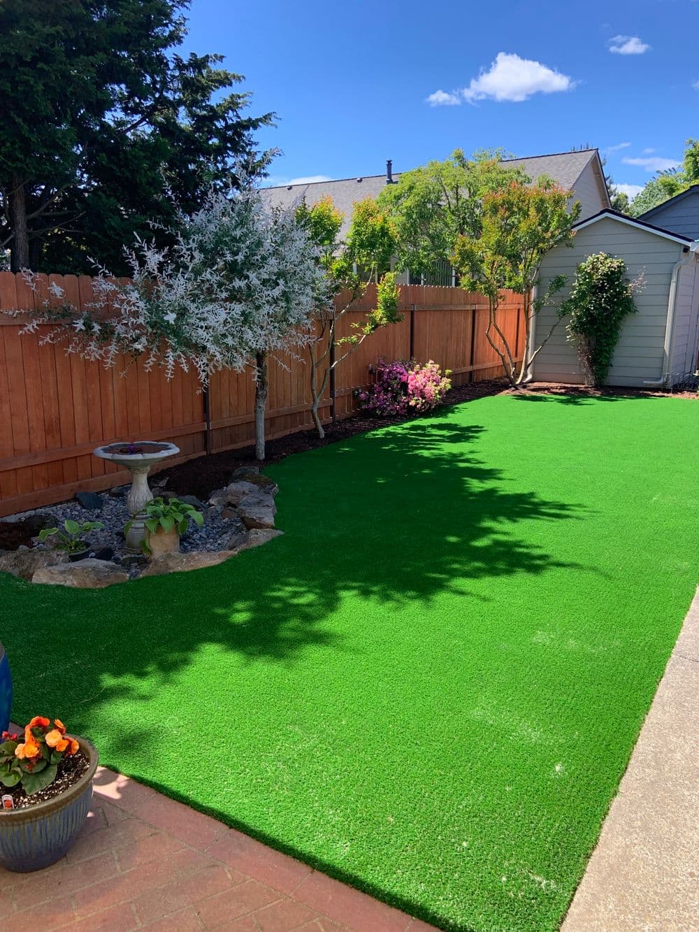 vibrant backyard with artificial turf, garden plants, and decorative birdbath under blue sky