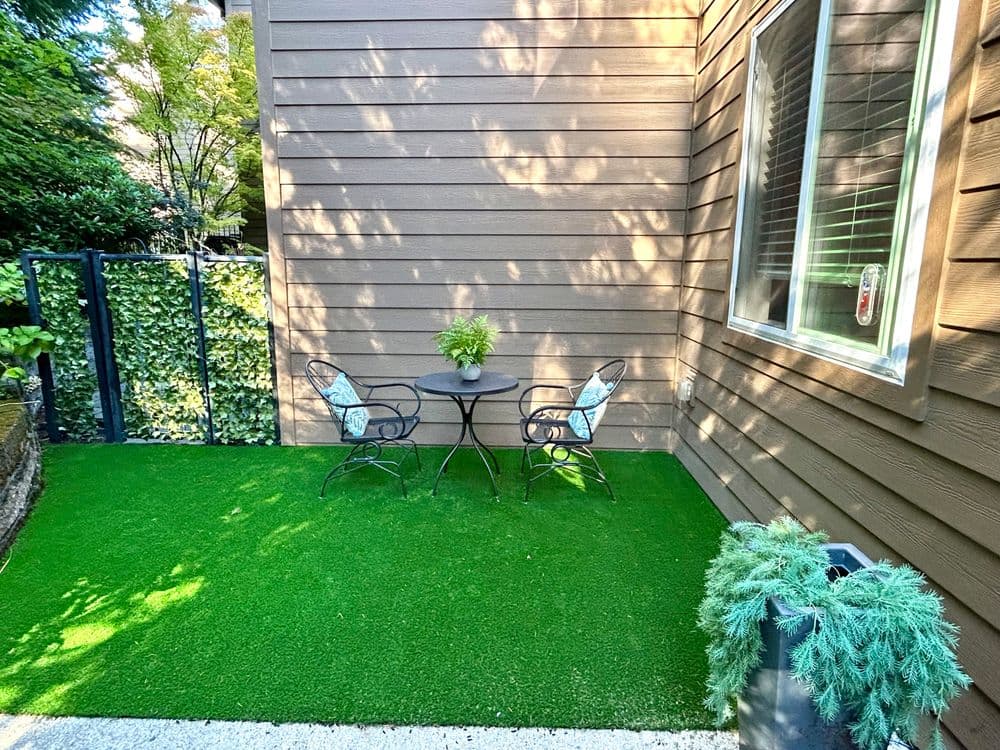 Cozy outdoor seating area with green artificial grass, table, and chairs beside a wooden wall.