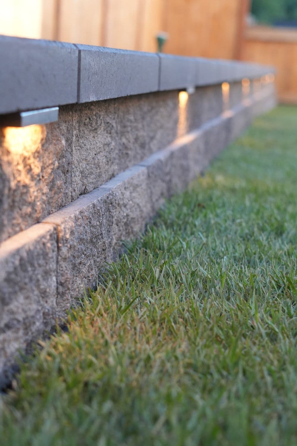 Landscape lighting on a stone wall with lush green grass in a backyard setting.