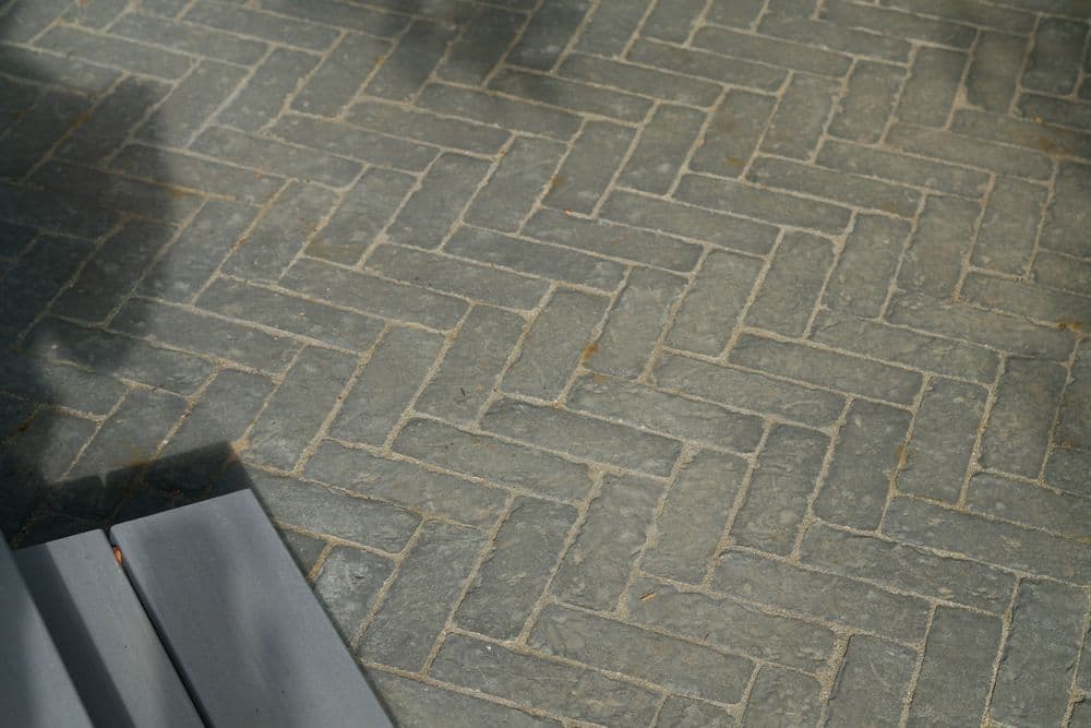Herringbone pattern gray stone flooring with shadows and wooden planks in view.