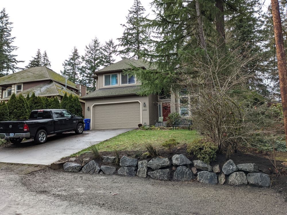 Two-story house with a front yard, parked black truck, and surrounding trees.