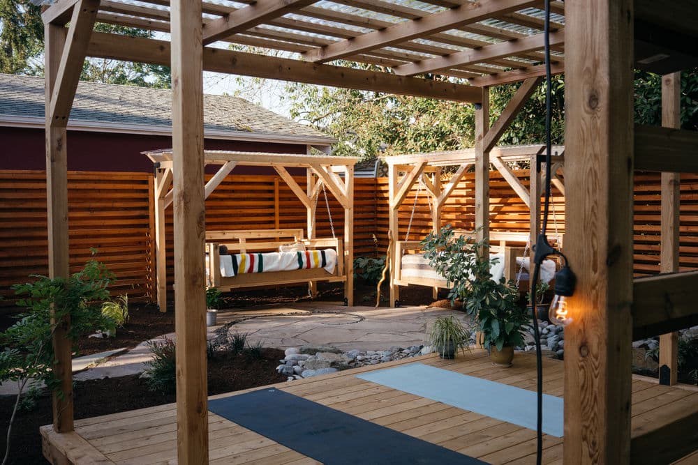 Stylish backyard retreat with wooden swings, stone path, and lush greenery. Relaxation space.