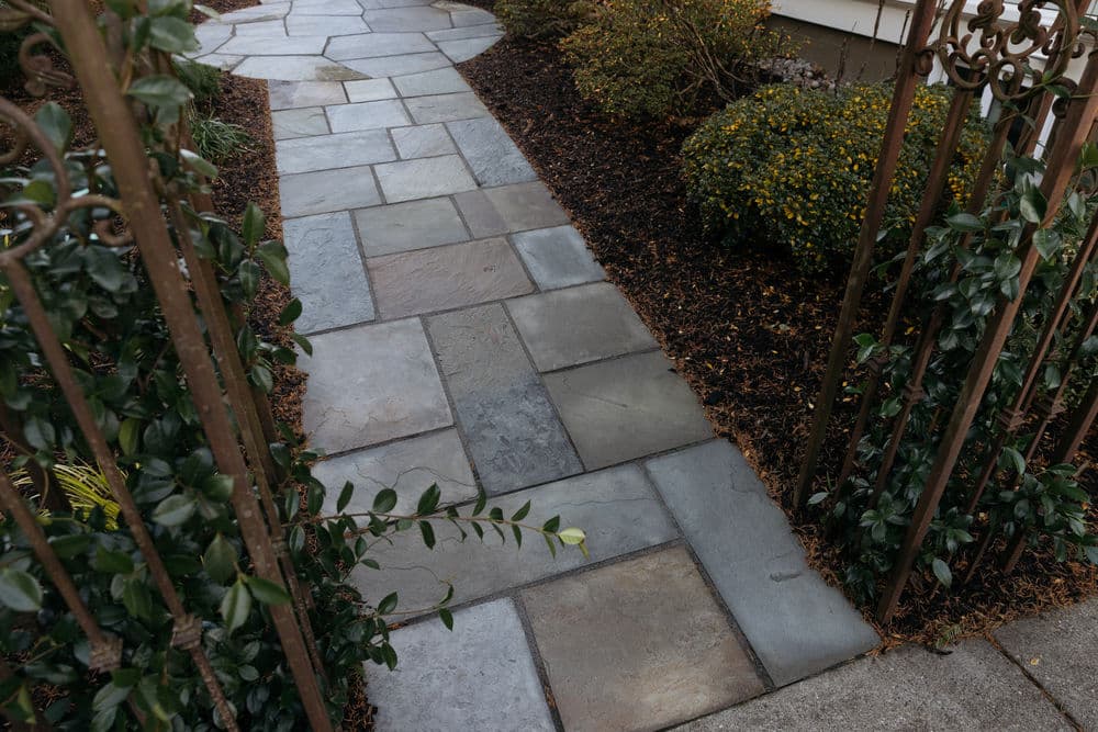 Stone pathway leading through an elegant wrought iron gate, surrounded by landscaped greenery.