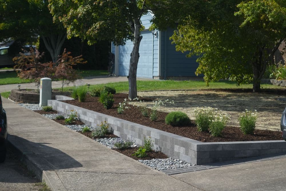 Modern landscaped garden with raised stone bed, shrubs, and gravel detailing, enhancing curb appeal.