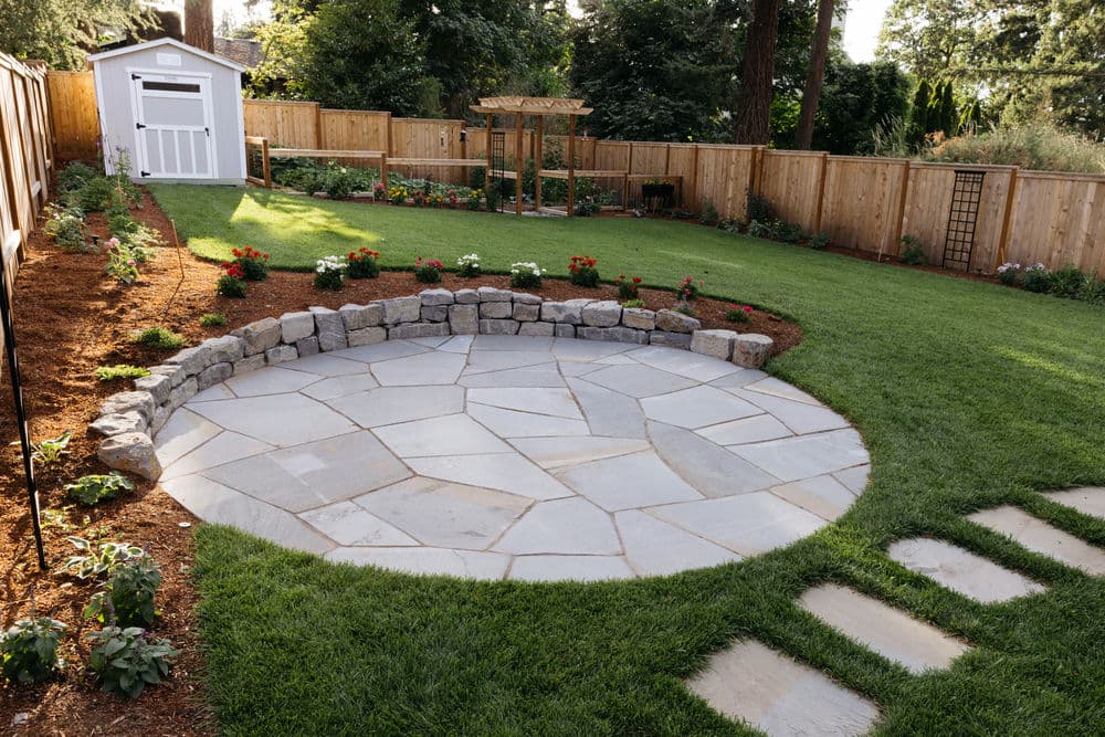 Backyard landscape featuring stone patio, flower beds, and a charming shed.