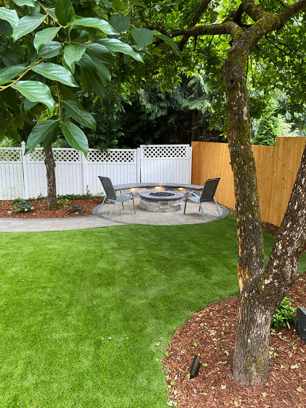 Cozy backyard fire pit area with seating, surrounded by green grass and wooden fence.