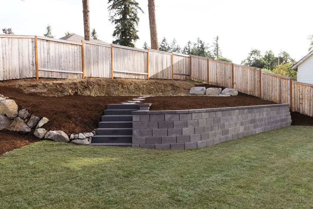 Landscaped backyard with tiered retaining wall, stone steps, and wooden fence.