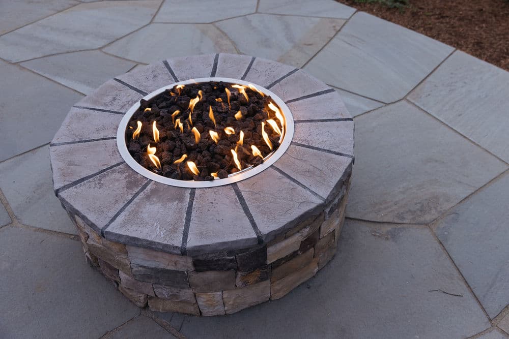 Modern stone fire pit with flames on a patio, surrounded by natural slate flooring.