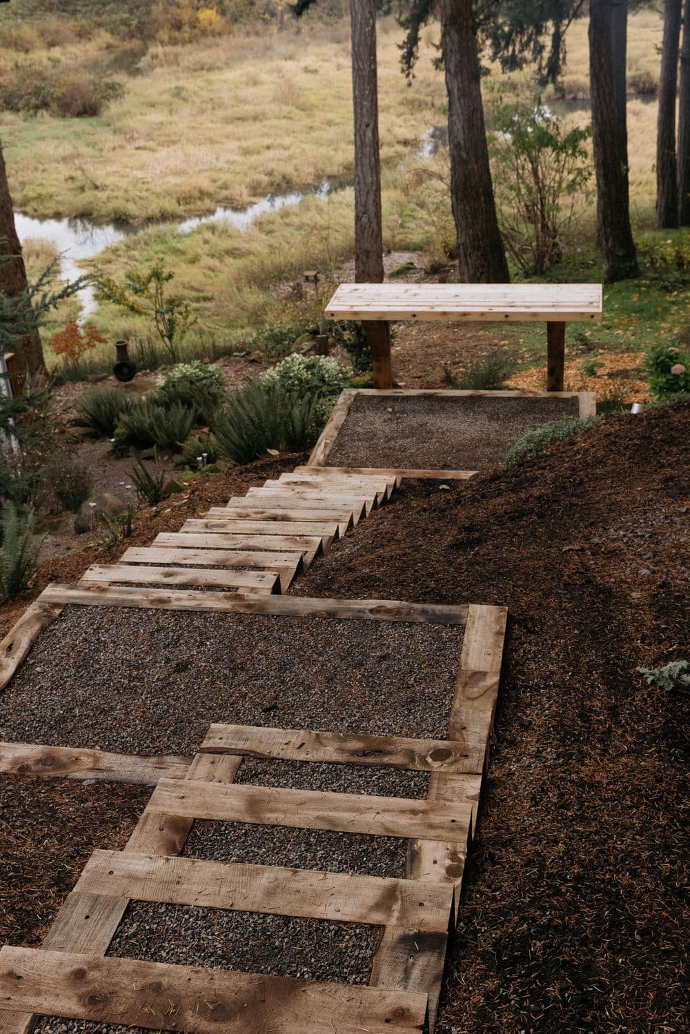 Wooden steps and landing overlook a grassy area near a river surrounded by trees.