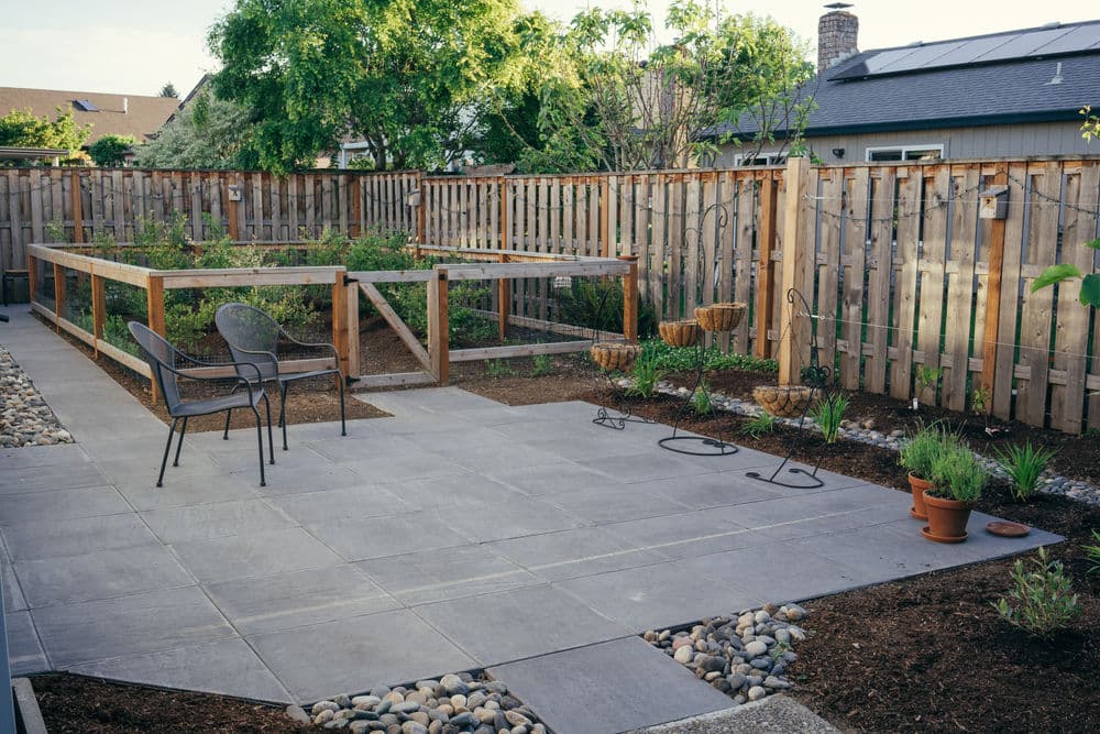 Modern garden with raised beds, stone patio, and seating area surrounded by wooden fence.
