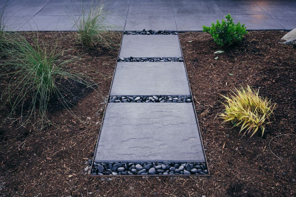 Modern garden pathway with stone slabs, pebbles, and lush green plants in landscape design.