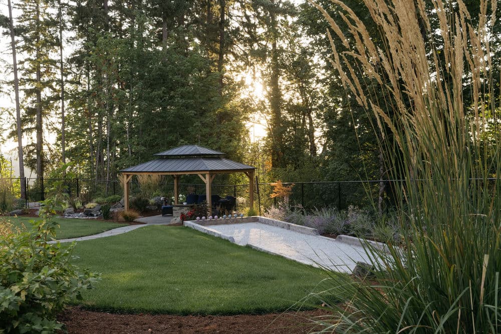 Serene backyard with gazebo, lush grass, and landscaped garden at sunset.