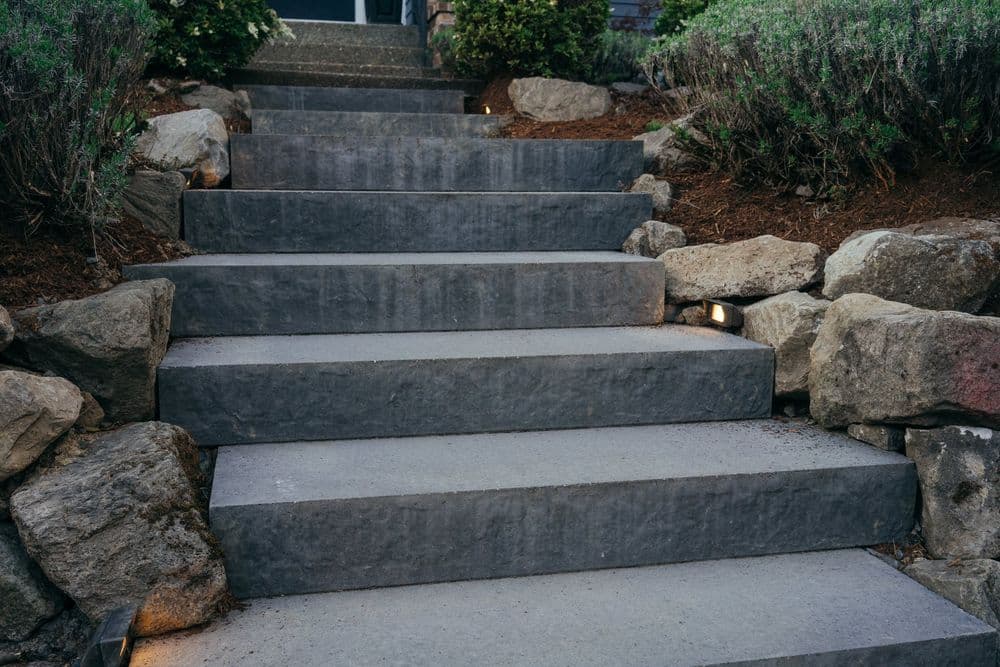 Modern stone stairs with LED lighting and surrounding greenery in a residential landscape.