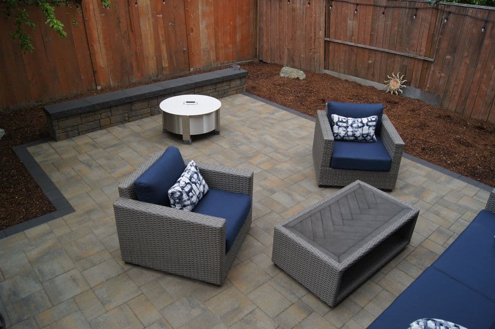Modern outdoor patio featuring wicker chairs, coffee table, and landscaped stone area.