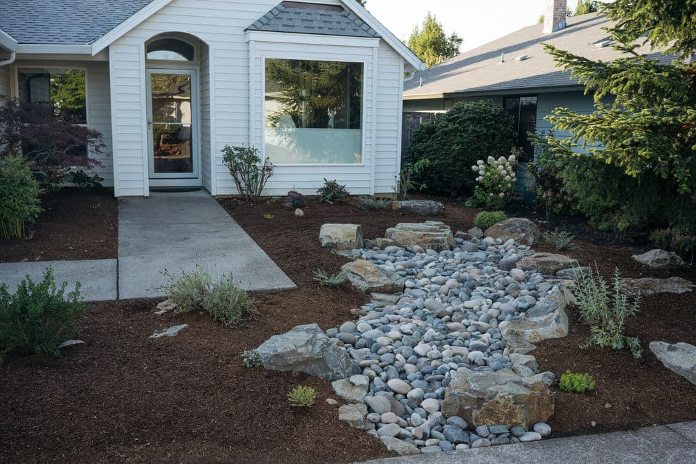 Front yard with a rock garden, creek bed, and low-maintenance landscaping featuring greenery.