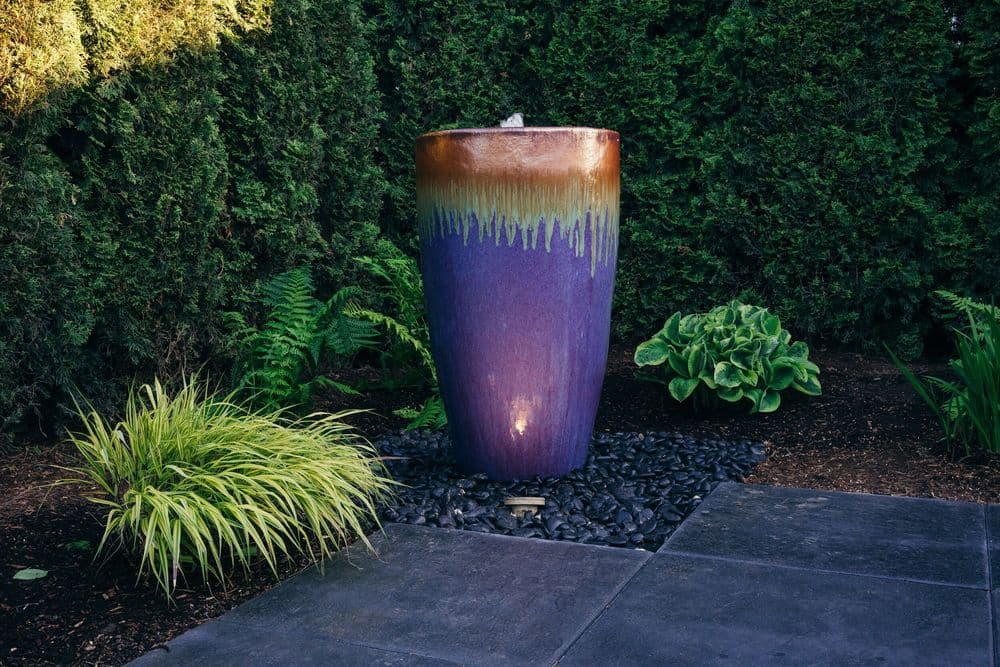 Colorful outdoor water fountain surrounded by lush greenery and stone landscaping.